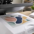 Pellicola stampata con un logo a colori appoggiata su una maglietta bianca prima del trasferimento a caldo